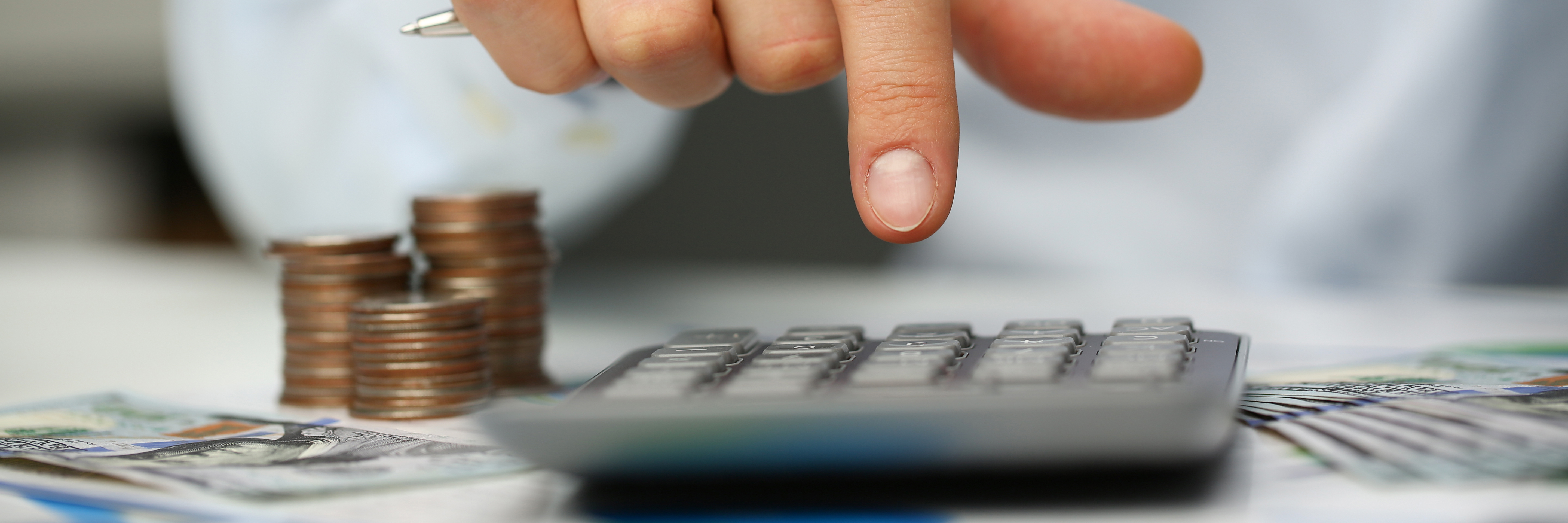 tres montones de monedas y un dedo pulsando una calculadora