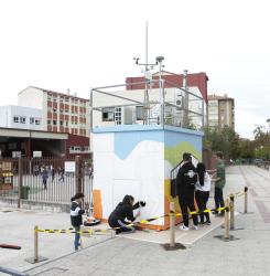 unos adolescentes pintando una cabina de medicion de la calidad del aire
