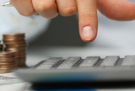 tres montones de monedas y un dedo pulsando una calculadora